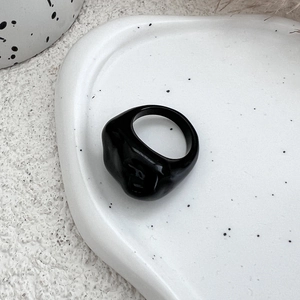 Detail of a minimalist irregular thick black resin ring on a white stone textured display