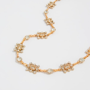 Close-up of golden geometric square links and round crystal inlays on metal waist chain