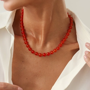Détail d'un collier de perles rouges translucides porté par un mannequin en chemise