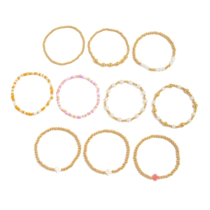 Détail de bracelets bohèmes en perles dorées avec croix en acrylique et perles nacrées