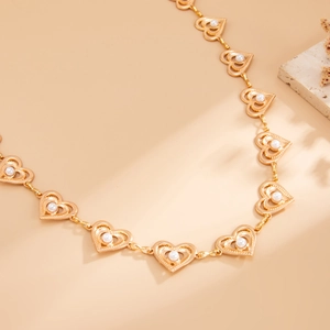 Detailed close-up of golden hollow heart links with white pearls on a minimalist warm background