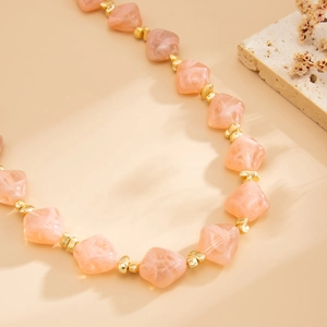 Macro detail of irregular pink marble resin beads and golden spacers on a stylish necklace