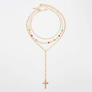 Dettaglio della collana a strati dorata con gemme colorate e un ciondolo a croce di cristallo