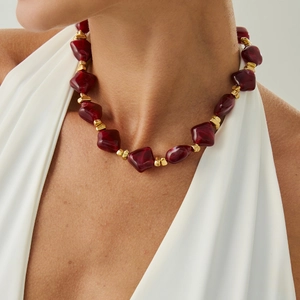 Close-up of irregular burgundy crystal resin beads with gold square spacers on a choker