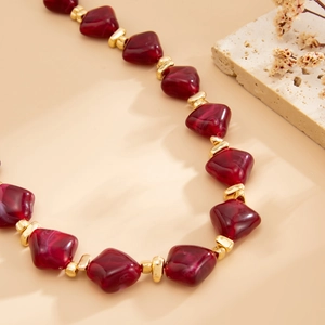 Detail of irregular burgundy resin beads with golden metal spacers on a choker necklace
