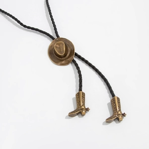 Detailansicht der bronzenen Cowboyhut-Schnalle und Vintage-Stiefelanhänger am Bolo-Tie