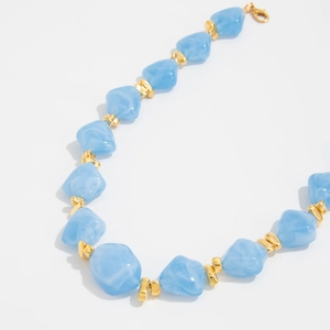 Detailed macro view of irregular light blue resin beads and gold metal spacers on necklace