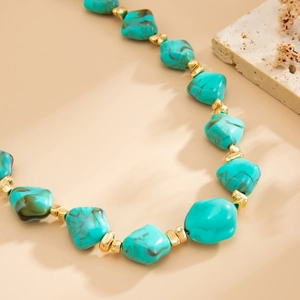 Macro detail of irregular turquoise resin beads with gold spacer accents on a choker necklace