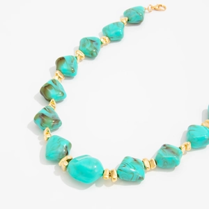 Detailed view of the irregular bluish resin beads and golden metallic spacers on the necklace