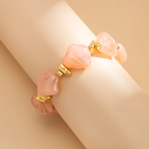 Detailed close-up of pink marble resin bracelet with gold beads on display stand
