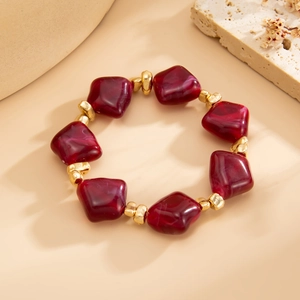 Detail view of irregular dark red resin beads and golden metal spacers on a beaded necklace