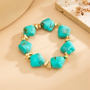 Macro detail of irregular turquoise resin beads with gold spacer accents on a stone surface