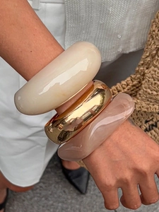Close-up of three thick resin and metal bracelets in cream, gold, and pink on a wrist