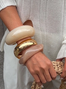 Close-up of stacked chunky resin and gold metal bracelets with marble textures