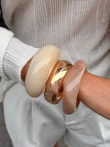 Macro detail of stacked oversized chunky resin and gold metal bracelets on model