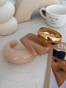 Chunky acrylic and gold resin bracelets shown on a minimalist decorative tabletop