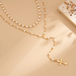 Detailweergave van gouden kruishanger ketting met witte parels en gelaagde Y-ketting