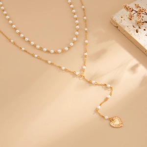 Detail van de gouden dubbellaagse ketting met witte parels en hartvormige hanger