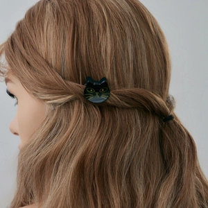 Détail d'une pince à cheveux chat noir avec détails jaunes sur cheveux ondulés