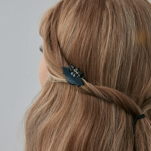 Détail d'une petite pince à cheveux chauve-souris noire sur cheveux châtains ondulés