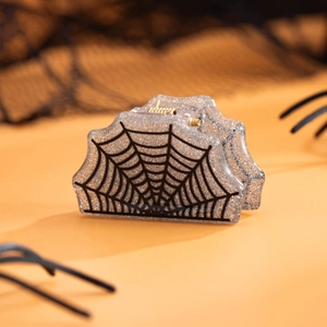 Détail de la pince à cheveux toile d'araignée scintillante avec ressort doré sur fond orange