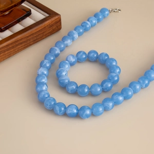 Detail von blau marmoriertem Acrylperlen-Halsketten- und Armband-Set auf beigem Hintergrund