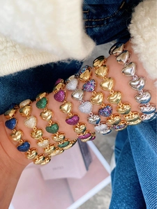 Détail de bracelets à maillons cœur superposés en or et argent avec zircons colorés