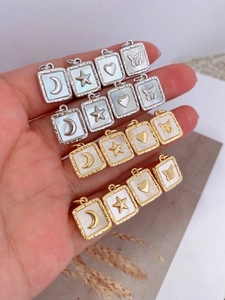 Macro detail of hand-held gold plated square mother of pearl pendants with celestial motifs