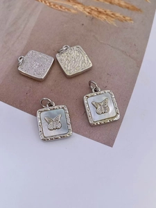 Detail of square gold-plated shell pendants with 3D butterfly design and pearl luster