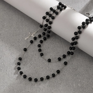Detail of cross pendant chain with black glossy beads and silver metal tassel links
