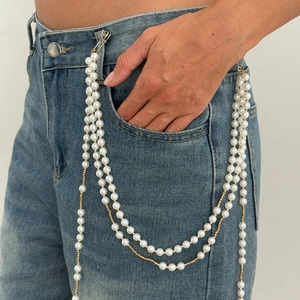 Detail of layered pearl and gold chain waist ornament with pins on denim jeans