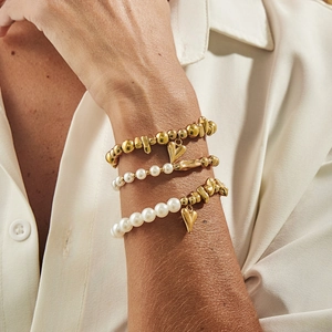 Detailansicht goldener Herzanhänger und Perlenarmbänder-Set am Handgelenk eines Models