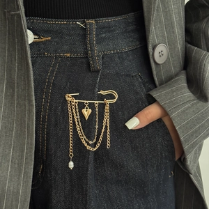 Detail of layered gold metal chain brooch with heart pendant and pearl on denim jeans