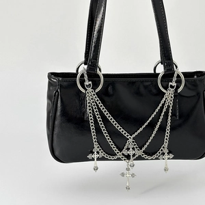 Detail of silver cross pendants and metal chains on a shiny black Y2K gothic handbag