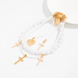 Detail view of multi-layer gold chain bag charm with white pearls and cross heart pendants