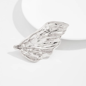 Détail d'une broche en métal argenté avec texture plissée irrégulière sur plateau