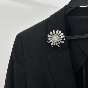 Détail d'une broche fleur argentée avec pétales superposés et cristaux sur une veste noire