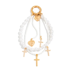Detail of faux pearl bag chain with golden cross pendants and heart charms on white background