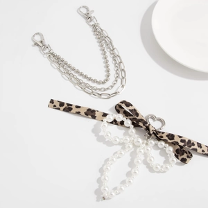 Detail of leopard print ribbon with pearl bow charm and multi-layer silver metal chain