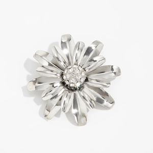 Détail d'une broche fleur argentée sertie de cristaux blancs sur un fond blanc épuré