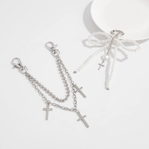 Detailed view of silver bow pearl charm and layered cross chain keychain for bags