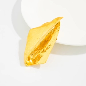 Détail d'une broche irrégulière dorée avec texture martelée sur une assiette blanche