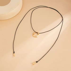Detalle de colgante circular irregular dorado en collar largo de cordón negro