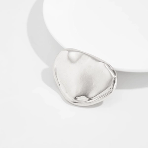 Détail macro d'une broche en métal liquide argenté avec texture froissée et fini miroir