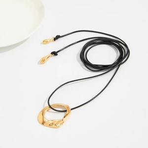 Detalle de collar dorado con colgante de lava y cordón negro sobre un plato blanco