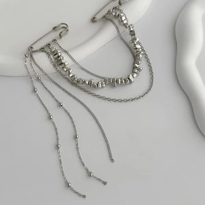 Detailed macro view of silver multi-layer chains and safety pin brooches with metallic beads