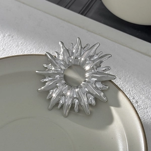 Détail d'une broche soleil en argent à texture métallique irrégulière sur un plat en céramique