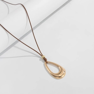 Detalle de un colgante de gota de oro hueco pulido en un collar de cordón marrón