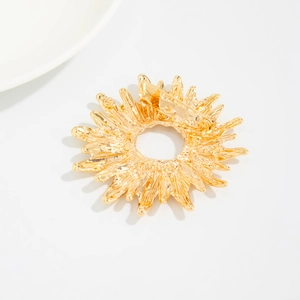 Détail d'une broche dorée en forme de soleil avec plis métalliques et épingle au dos