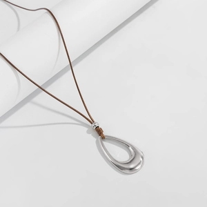 Primer plano de un colgante de gota hueca de plata en un collar de cordón marrón